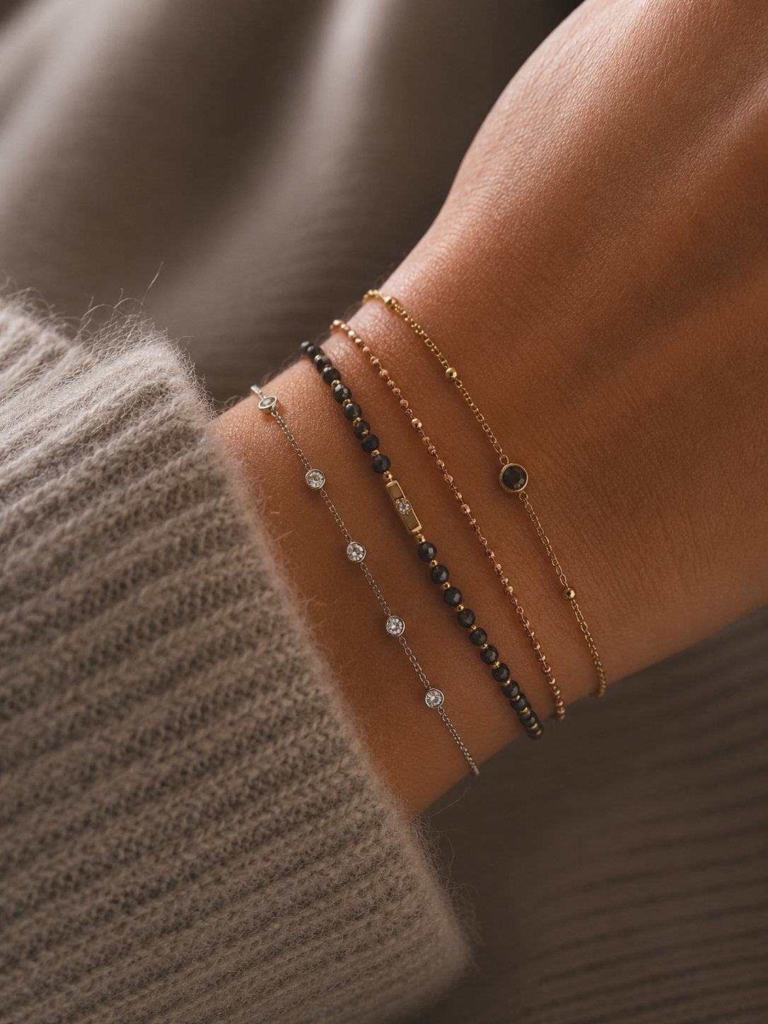 Bracelet Mona argenté avec petits zirconiums lumineux porté sur un poignet féminin en maille douce beige taupe