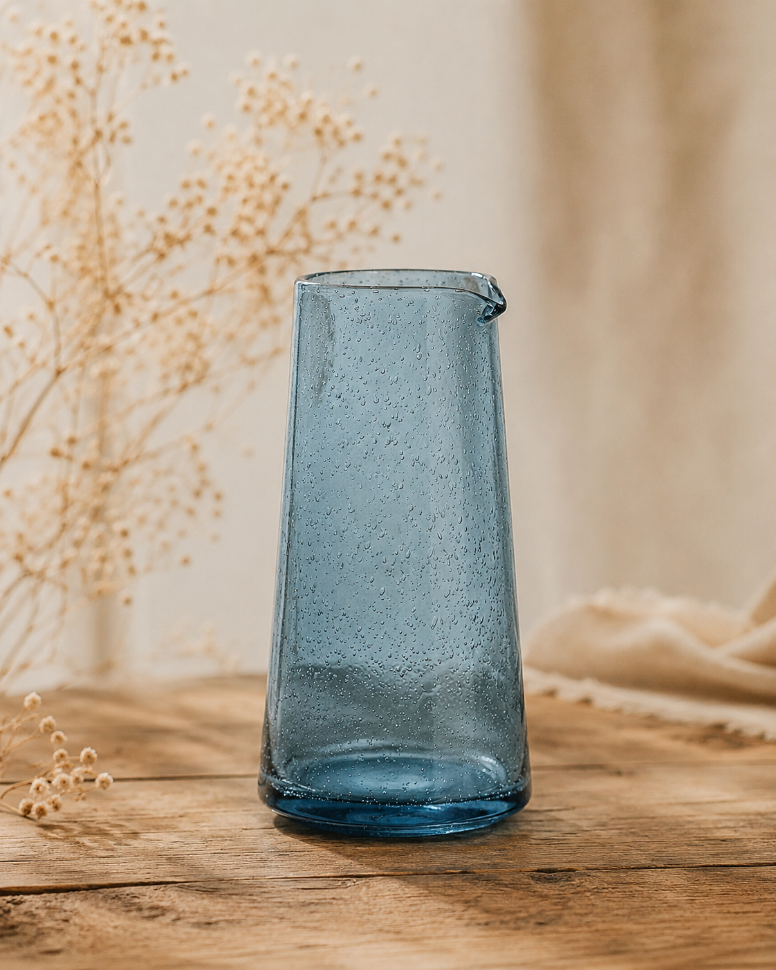 Pichet en verre bullé bleu artisanal posé sur une table en bois dans une ambiance décoration naturelle et chaleureuse