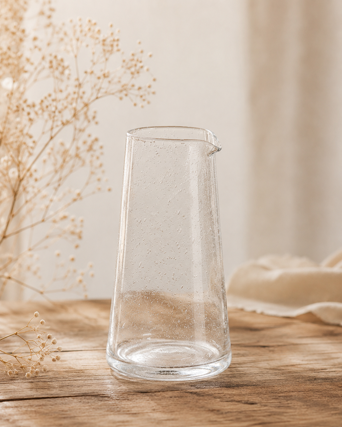 Pichet en verre bullé transparent artisanal posé sur une table en bois dans une ambiance décoration naturelle et chaleureuse