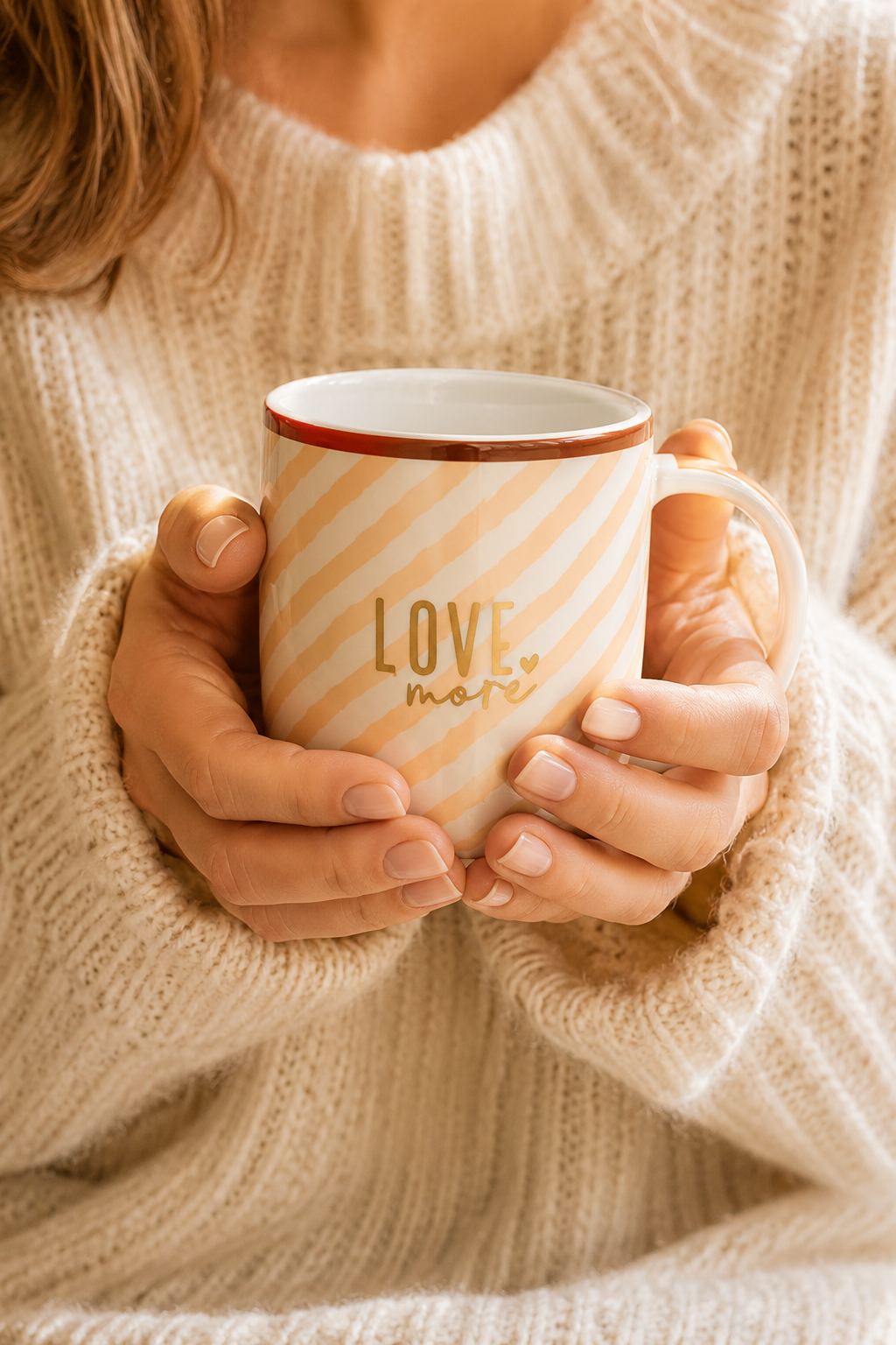 Femme tenant un mug Love More en porcelaine rayures beige rosé dans une ambiance cosy et chaleureuse