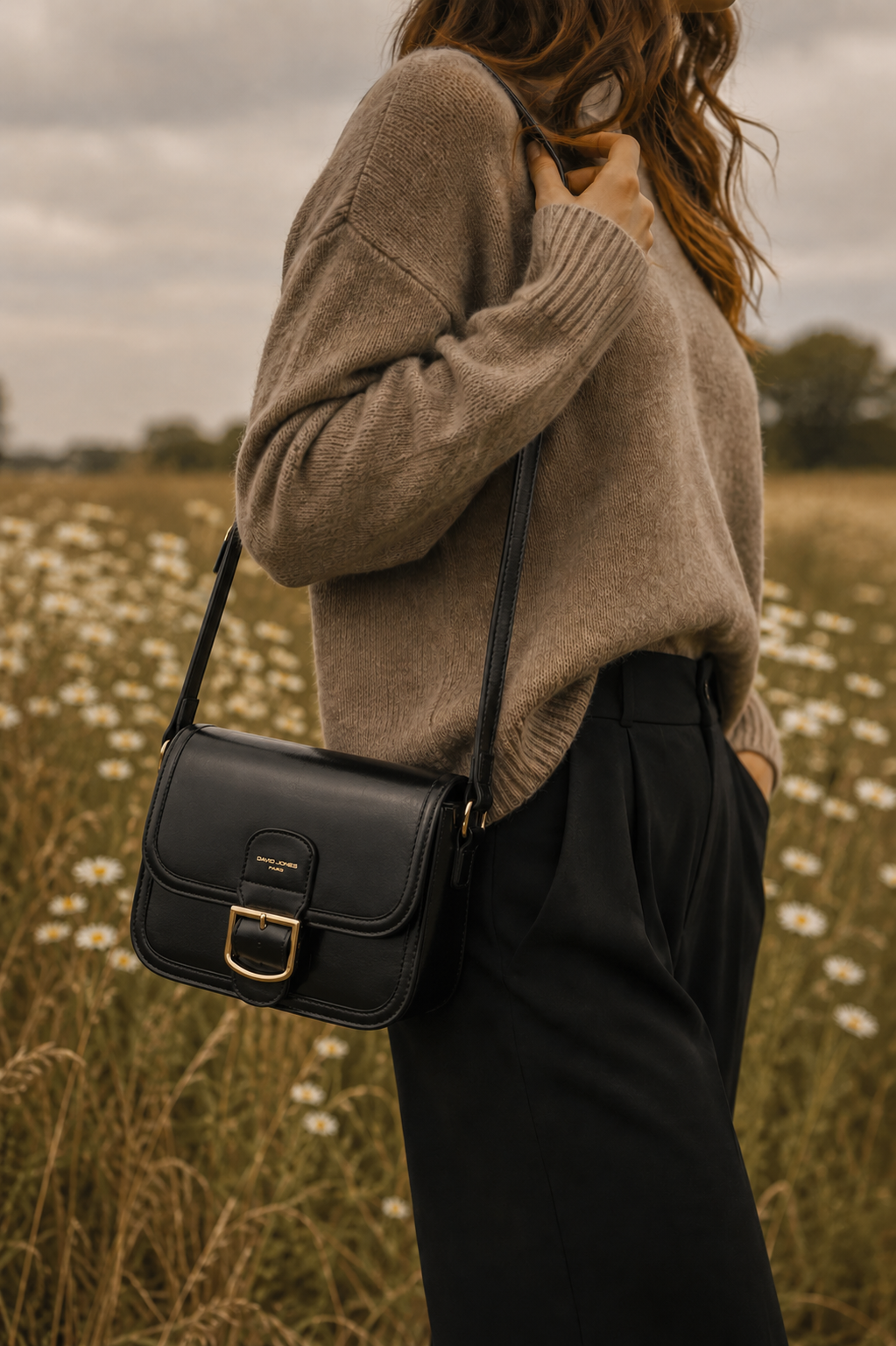 Femme portant le sac bandoulière noir Amy en similicuir lisse avec boucle dorée dans un paysage naturel élégant et chaleureux