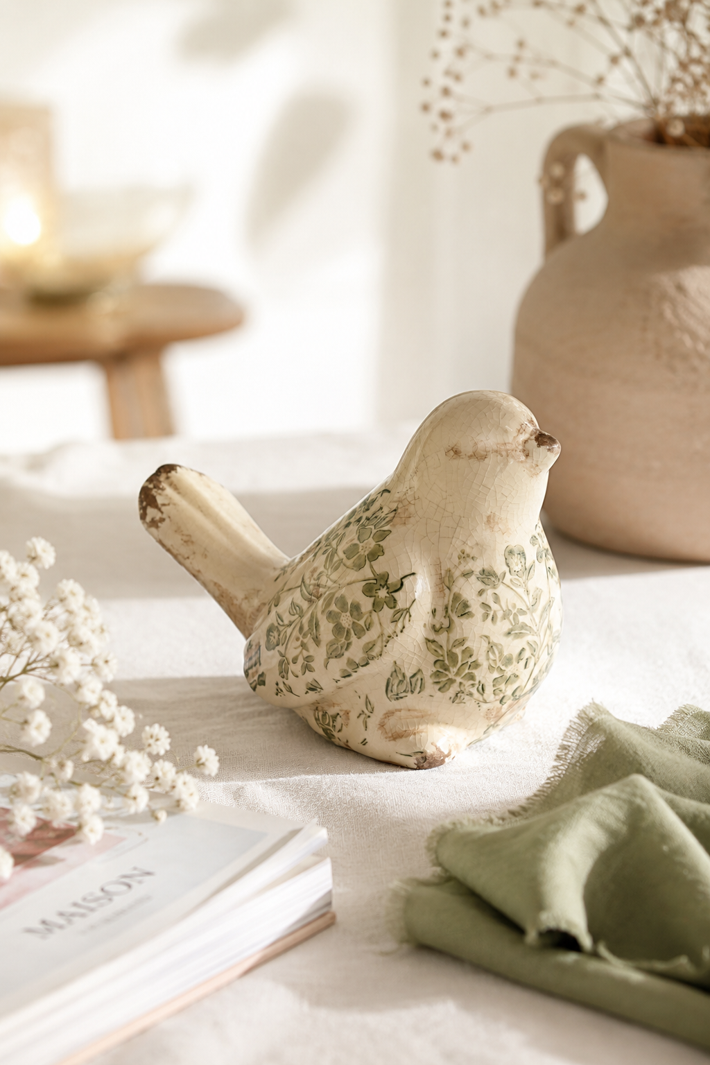 Figurine oiseau décorative en grès émaillé avec motif feuillage vert, posée sur une table en lin dans une décoration naturelle et chaleureuse.