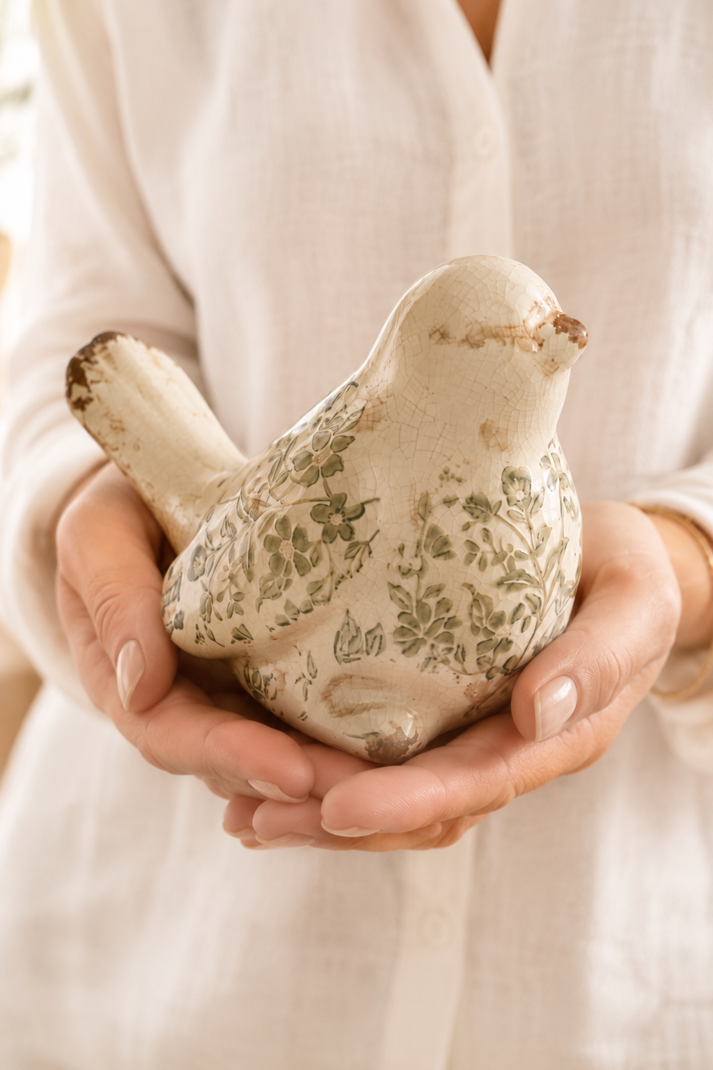 Figurine oiseau décorative en grès émaillé à motif feuillage vert tenue dans les mains pour montrer sa taille réelle dans une ambiance naturelle et chaleureuse.