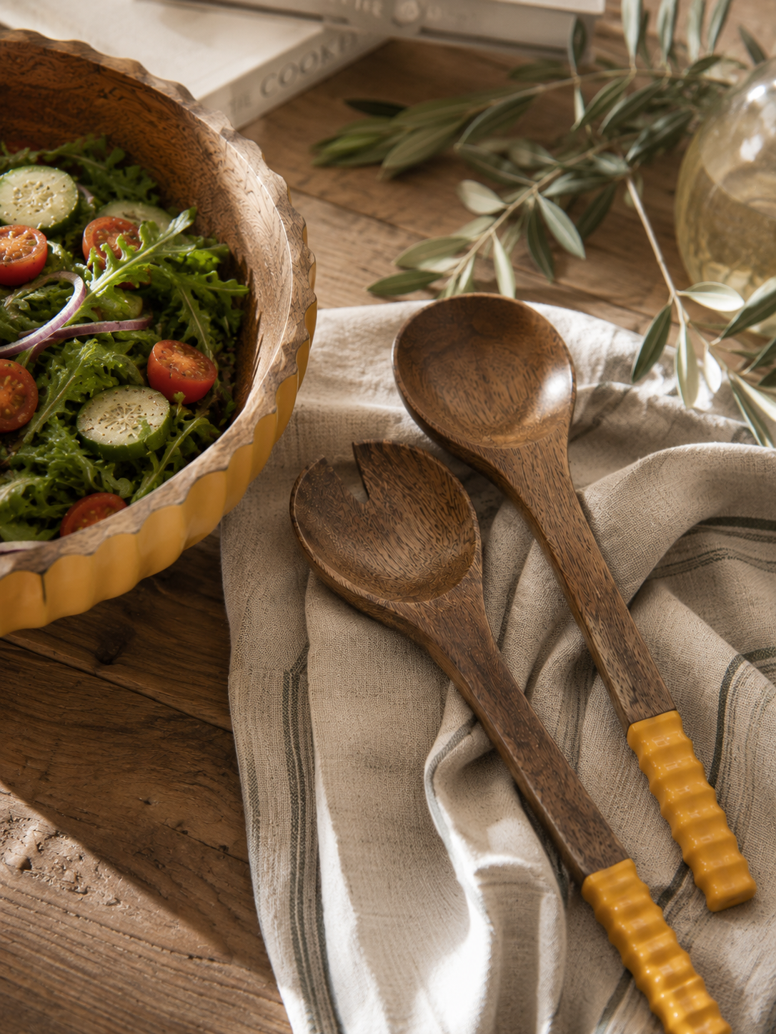 Couverts à salade en bois de manguier assortis au saladier de la collection naturelle Bella Cosa, présentés dans une ambiance chaleureuse sur une table de cuisine.