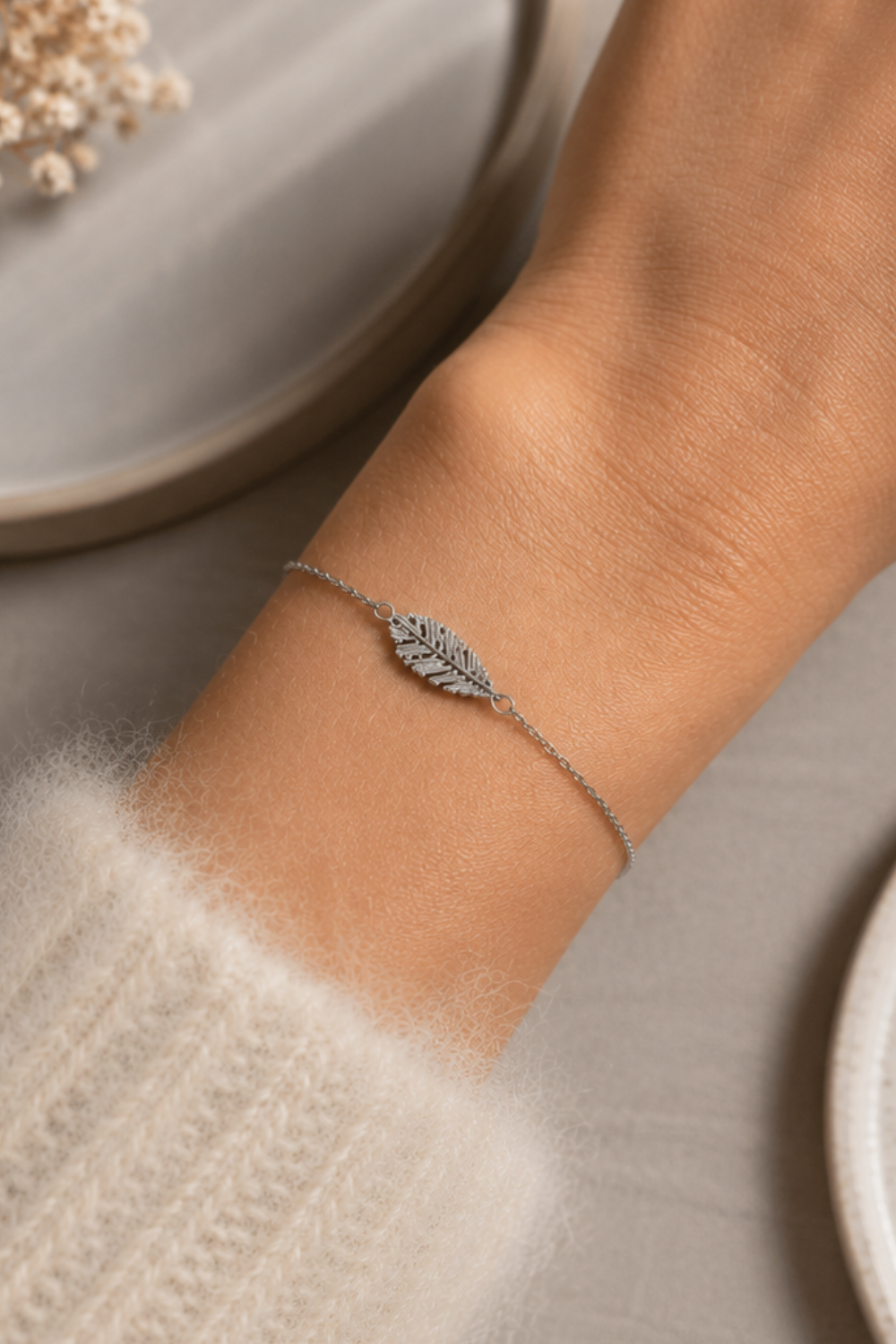 Bracelet Flora argenté en acier inoxydable porté au poignet, bijou fin avec feuille délicate dans une ambiance douce et élégante.