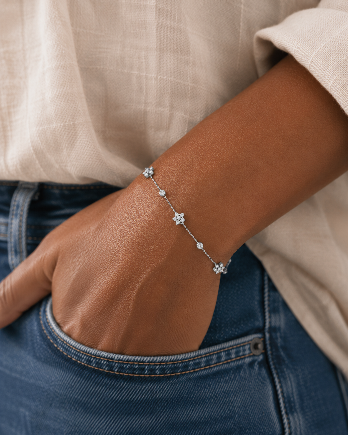 Bracelet Ellie argenté en acier inoxydable porté à la main dans une poche de jean, bijou fin avec fleurs et cristaux dans un style naturel et élégant.