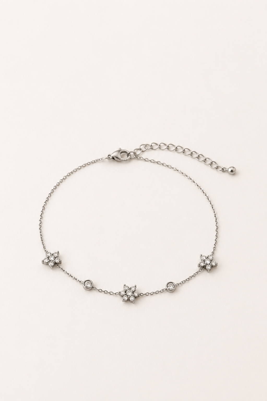 Bracelet Ellie argenté en acier inoxydable avec fleurs et cristaux sur fond beige clair, bijou fin et élégant pour femme.