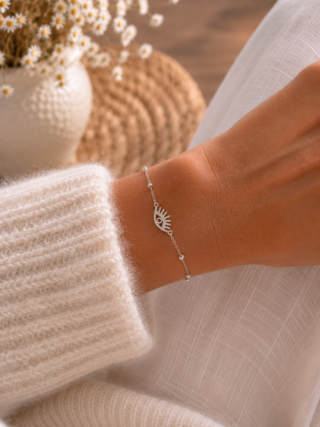 Bracelet Lorine argenté en acier inoxydable porté au poignet, avec œil protecteur ajouré et perles blanches, dans une ambiance naturelle et élégante.