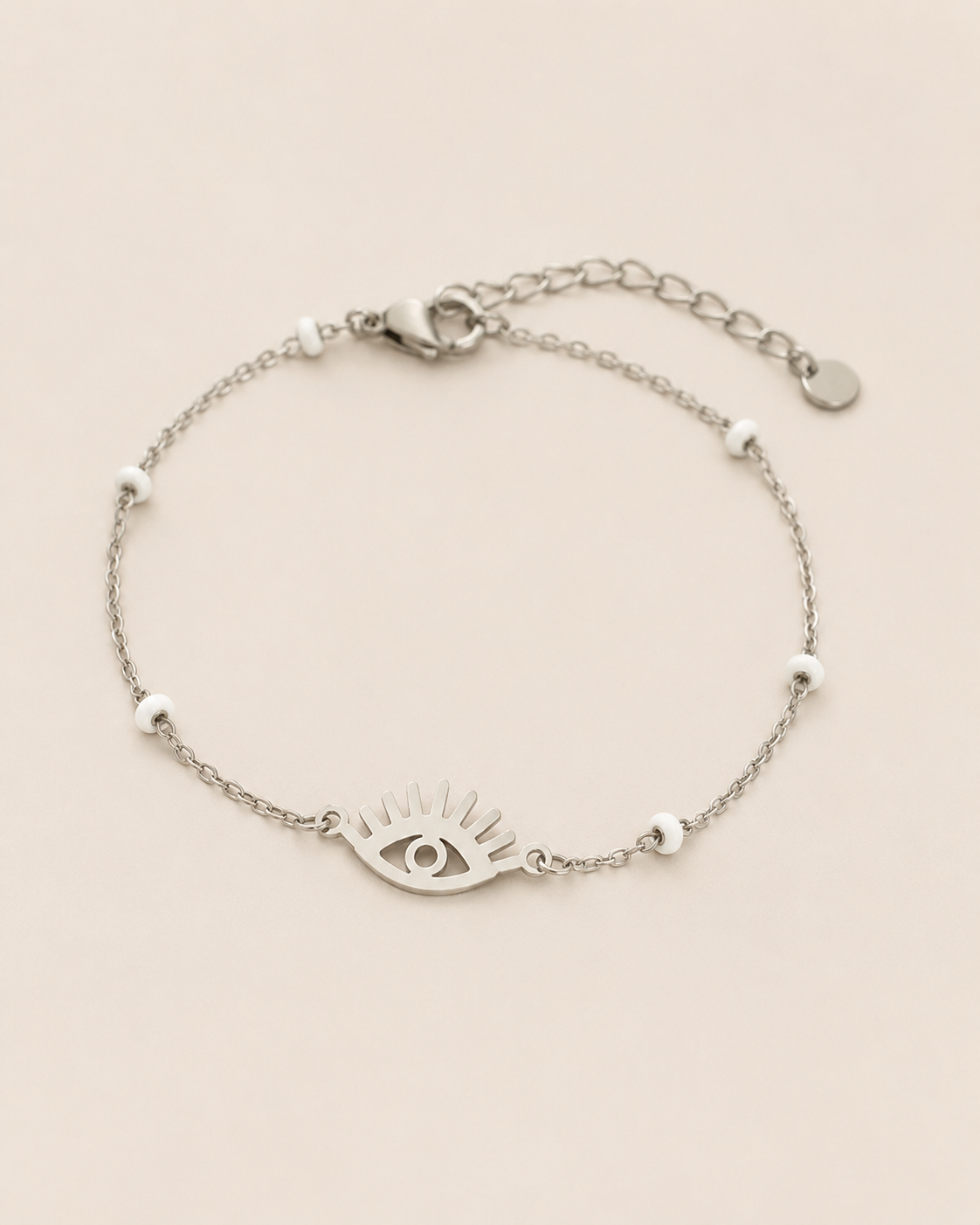 Bracelet Lorine argenté en acier inoxydable avec œil protecteur ajouré et perles blanches sur fond beige clair, bijou fin et élégant pour femme.