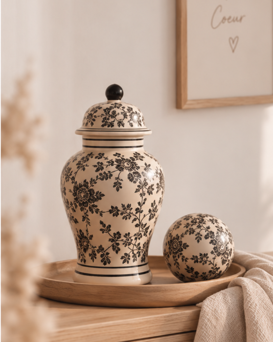 Vase Tibor en grès écru à motifs floraux noirs avec son couvercle et sa boule décorative assortie sur un plateau en bois.