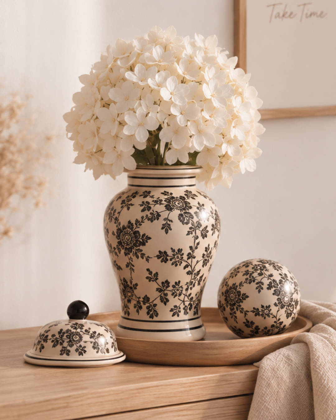 Vase Tibor en grès écru à motifs floraux noirs utilisé avec un hortensia blanc, accompagné de la boule décorative assortie.