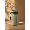 Thermos isotherme vert sauge sur fond uni beige chaud avec lumière naturelle tamisée et ambiance cosy premium inspirée du slow living et de la décoration scandinave chaleureuse