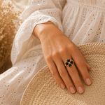 Main portant la bague Banga noire et dorée avec robe en broderie anglaise et panier tressé – bijou femme élégant Bella Cosa