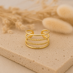 Bague Orane dorée à quatre rangs posée sur pierre naturelle beige avec arrière-plan flouté – bague femme Bella Cosa