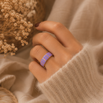 Main portant la bague Vic violette et dorée avec pull mohair beige dans une ambiance douce et élégante – bijou femme Bella Cosa