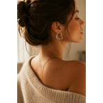 Femme brune portant les boucles d’oreilles Prya argentées en forme de cœur dans une ambiance douce et lumineuse