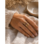 Main portant la bague Valéria dorée et violette dans une ambiance douce et naturelle aux tons beige et caramel – bijou femme Bella Cosa