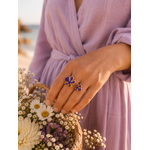 Main portant la bague Vélina dorée avec pierre violette dans une ambiance chic et moderne aux tons beige et doré – bijou femme Bella Cosa