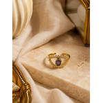 Bague Victoria dorée avec pierre violette posée sur travertin beige et tissu naturel dans une ambiance chic et chaleureuse – Bella Cosa