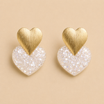Boucles d’oreilles Caroline blanc glacier cœur pailleté et doré sur fond beige minimaliste