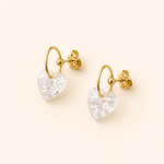 Boucles d’oreilles Cassie blanc glacier avec cœur translucide pailleté sur fond beige doux