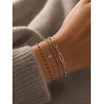 Bracelet Ginnie argenté à maille trombone porté sur un poignet féminin avec accumulation de bracelets fins argentés