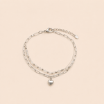 Bracelet April argenté double rang avec perles blanches et pendentif cœur sur fond crème minimaliste