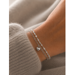 Bracelet April argenté double rang avec perles blanches et pendentif cœur porté sur un poignet féminin en maille douce beige taupe