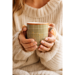 Femme tenant un mug en porcelaine kaki quadrillage terracotta dans une ambiance cosy et chaleureuse  ou