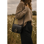 Femme portant le sac bandoulière noir Amy en similicuir lisse avec boucle dorée dans un paysage naturel élégant et chaleureux