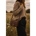 Femme portant le sac bandoulière marron Amy en similicuir lisse avec boucle dorée dans un paysage naturel élégant et chaleureux