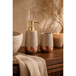 Set de salle de bain texturé beige minéral et cuivre rosé avec distributeur à savon et gobelet assorti dans une ambiance spa chaleureuse et élégante sur meuble en bois foncé
