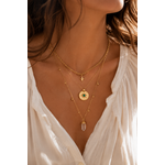 Femme portant le collier Patti double chaîne dorée avec pendentif astral et pierre verte dans une ambiance bohème chic lumineuse et élégante