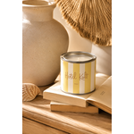 Bougie artisanale parfumée senteur monoï dans un pot style peinture rayé jaune et blanc posée sur des livres dans une décoration chaleureuse slow living