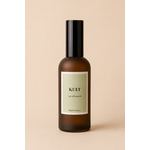 Parfum de maison senteur lait d’amande douce en verre ambré avec étiquette vert doux sur fond uni beige chaleureux