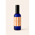 Brume de maison senteur fleur d’oranger en verre bleu fumé avec étiquette rayée orange et crème sur fond uni blanc chaud minimaliste