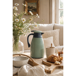 Thermos isotherme vert sauge sur table basse en bois clair dans un intérieur cosy avec pâquerettes naturelles, tasse en céramique et ambiance slow living élégante