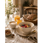 Bol en faïence ivoire présenté sur une table de petit-déjeuner chaleureuse avec café mousseux, jus d'orange, pain artisanal et fruits rouges