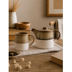 Mug et théière Arya en grès émaillé et grès brut dans une ambiance chaleureuse, sur une table en bois naturel pour un moment thé ou café.