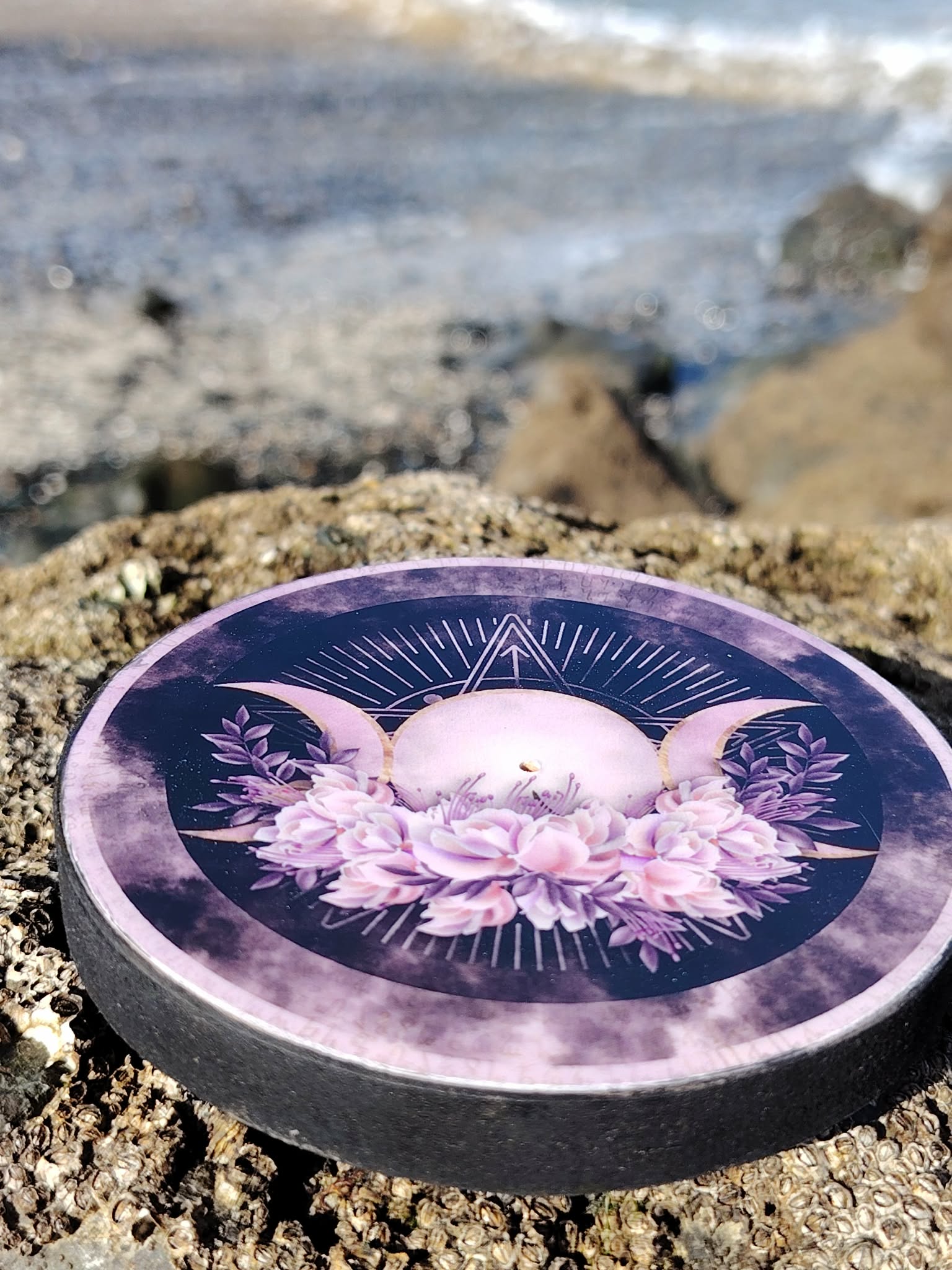 Brûleur d’encens violet motif Triple Lune posé sur un rocher face à la mer en Bretagne, idéal pour une fumigation douce et une ambiance apaisante