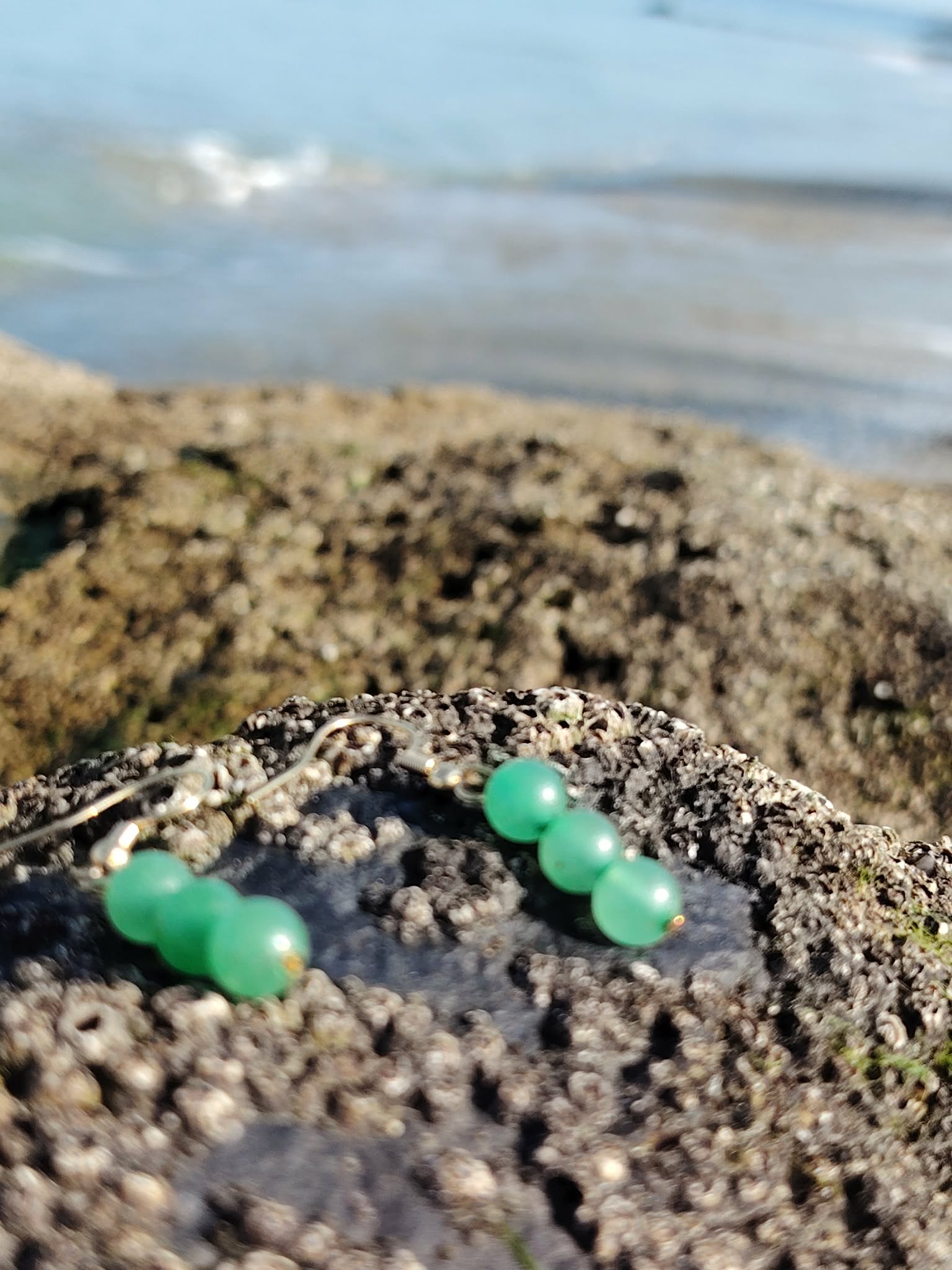 Boucles d’oreilles en aventurine verte, création Magic Gaïa, sur rocher au bord de mer en Bretagne avec horizon bleu, pour apaisement et optimisme.