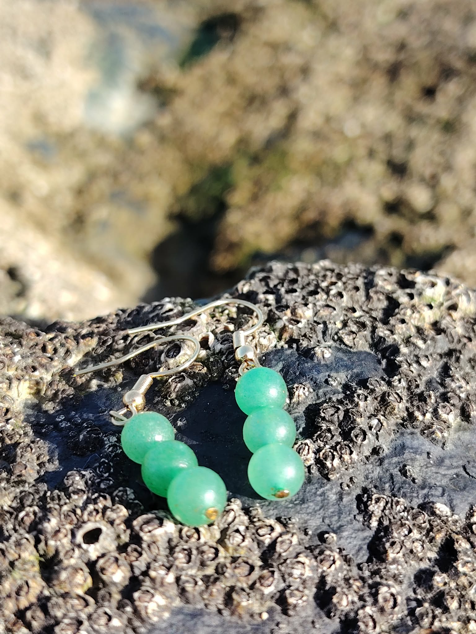 Boucles d’oreilles en aventurine verte, création Magic Gaïa, posées dans une anfractuosité de rocher en bord de mer en Bretagne, pour apaisement et optimisme.