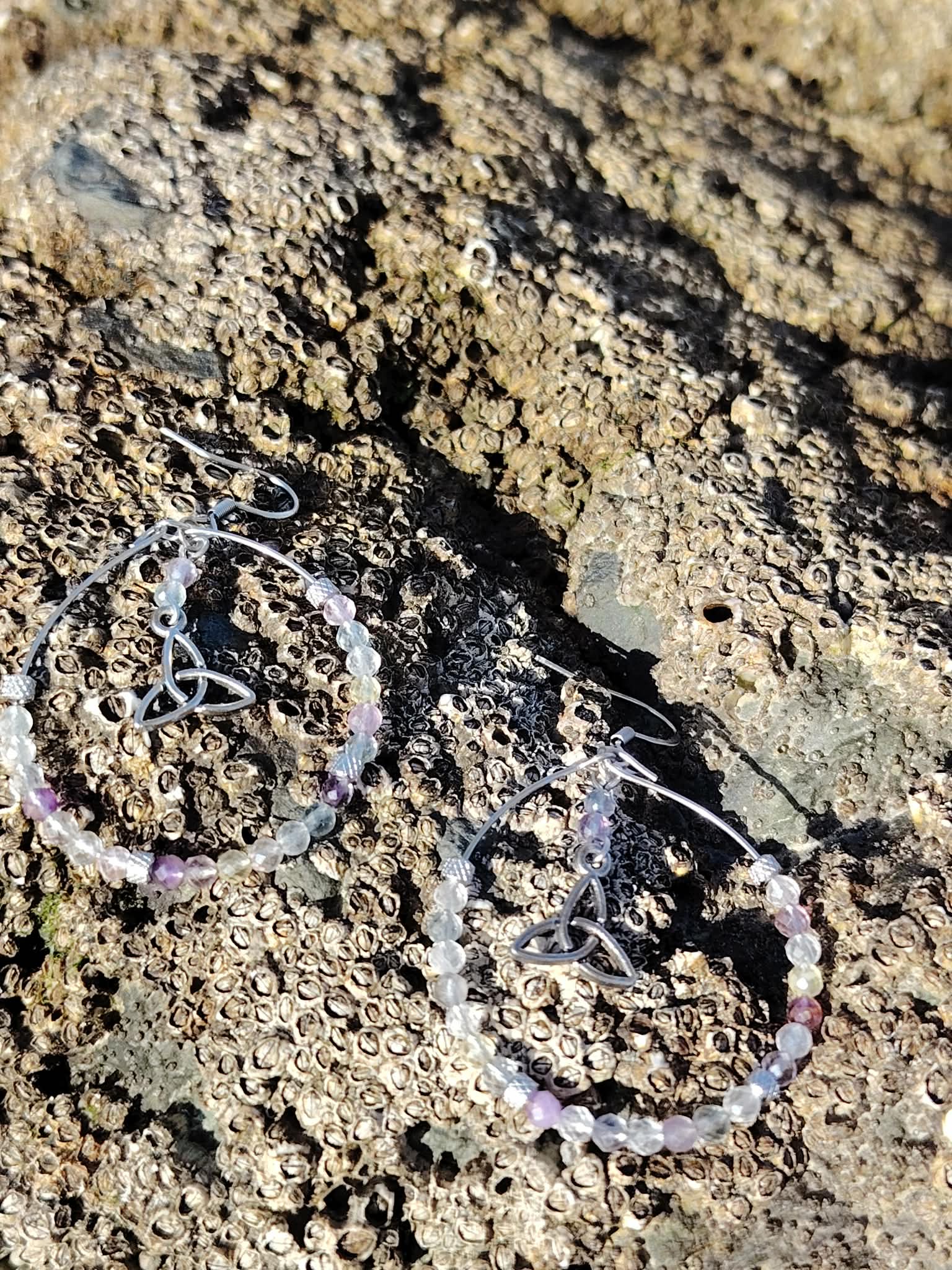Boucles d’oreilles Hécate en fluorite, création Magic Gaïa, photographiées sur rocher breton aux textures brutes, pour clarté intérieure et apaisement.