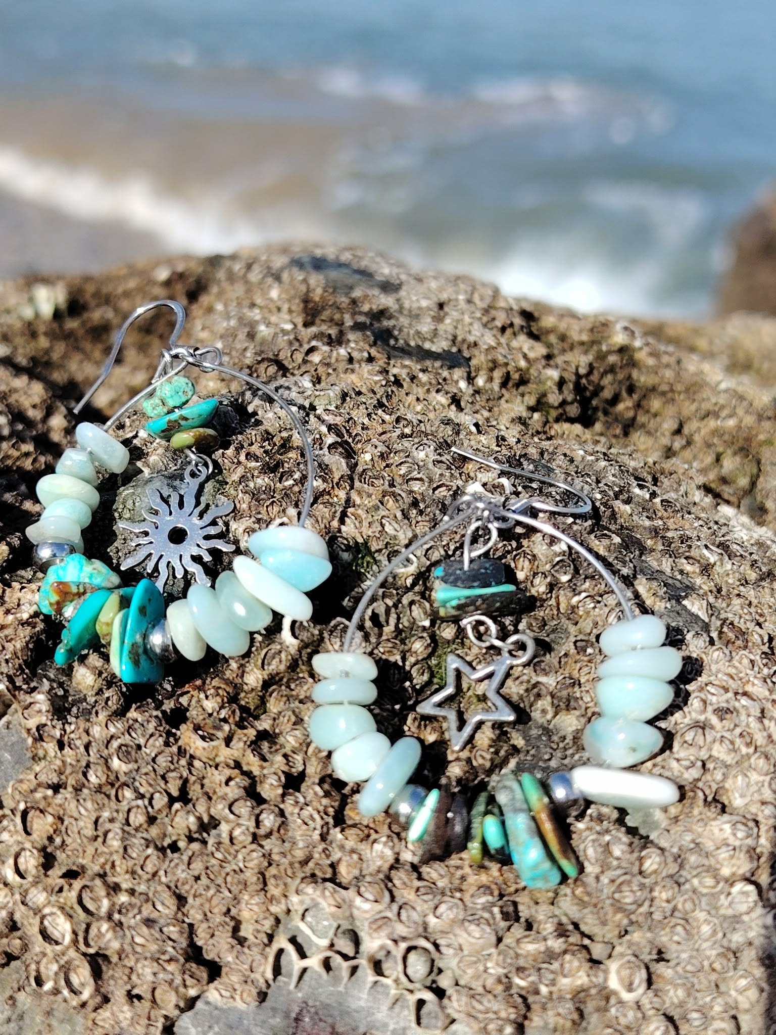 Boucles d’oreilles Ombre et Lumière, création Magic Gaïa, perles turquoise et blanches avec breloques, photographiées sur rocher en Bretagne face à la mer.
