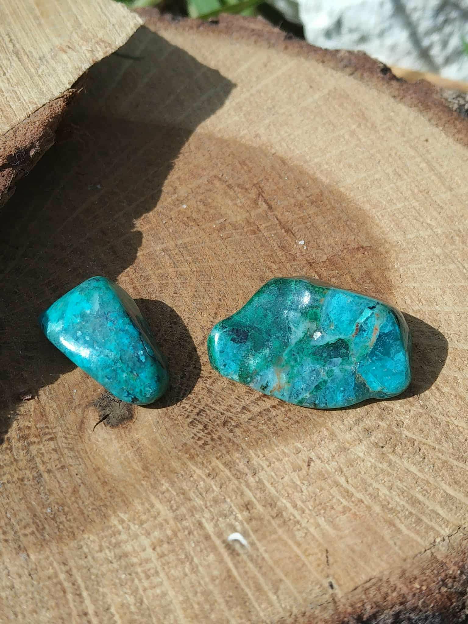 Deux galets de chrysocolle bleu-vert sur bois clair avec ombre douce, pierres roulées aux reflets lumineux liées au discernement, à la paix intérieure et à la présence à soi.