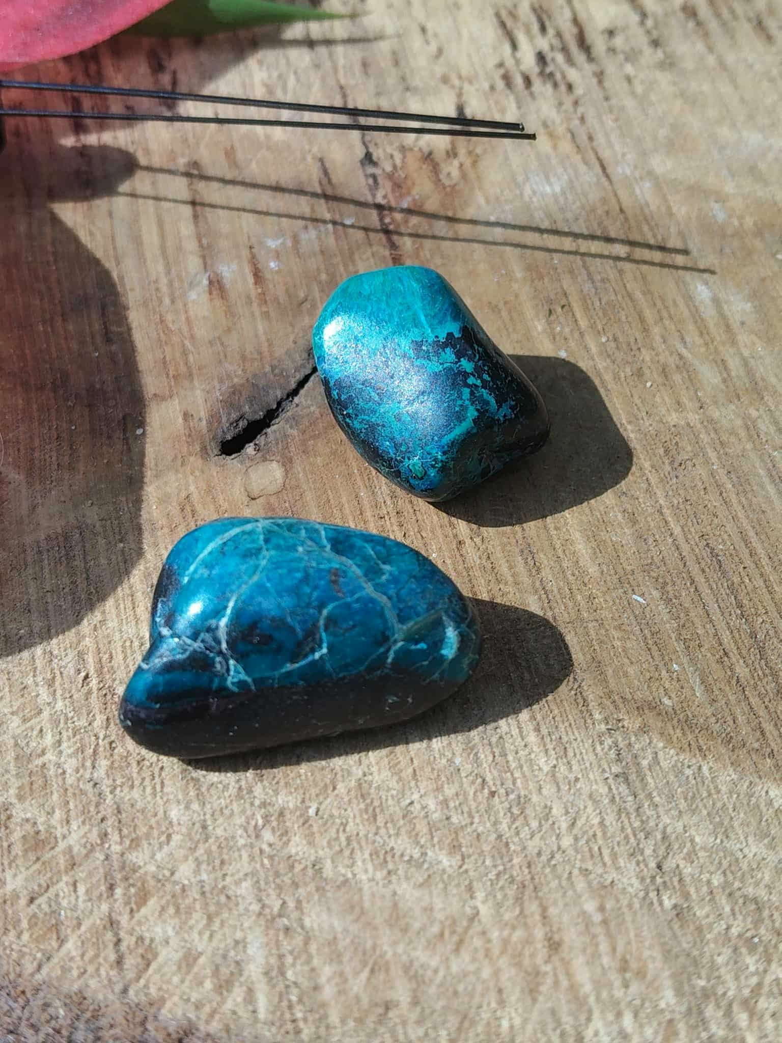 Deux galets de chrysocolle bleu-vert posés sur bois clair en photo minimaliste, pierres roulées évoquant la lucidité, la stabilité émotionnelle et une communication sereine.
