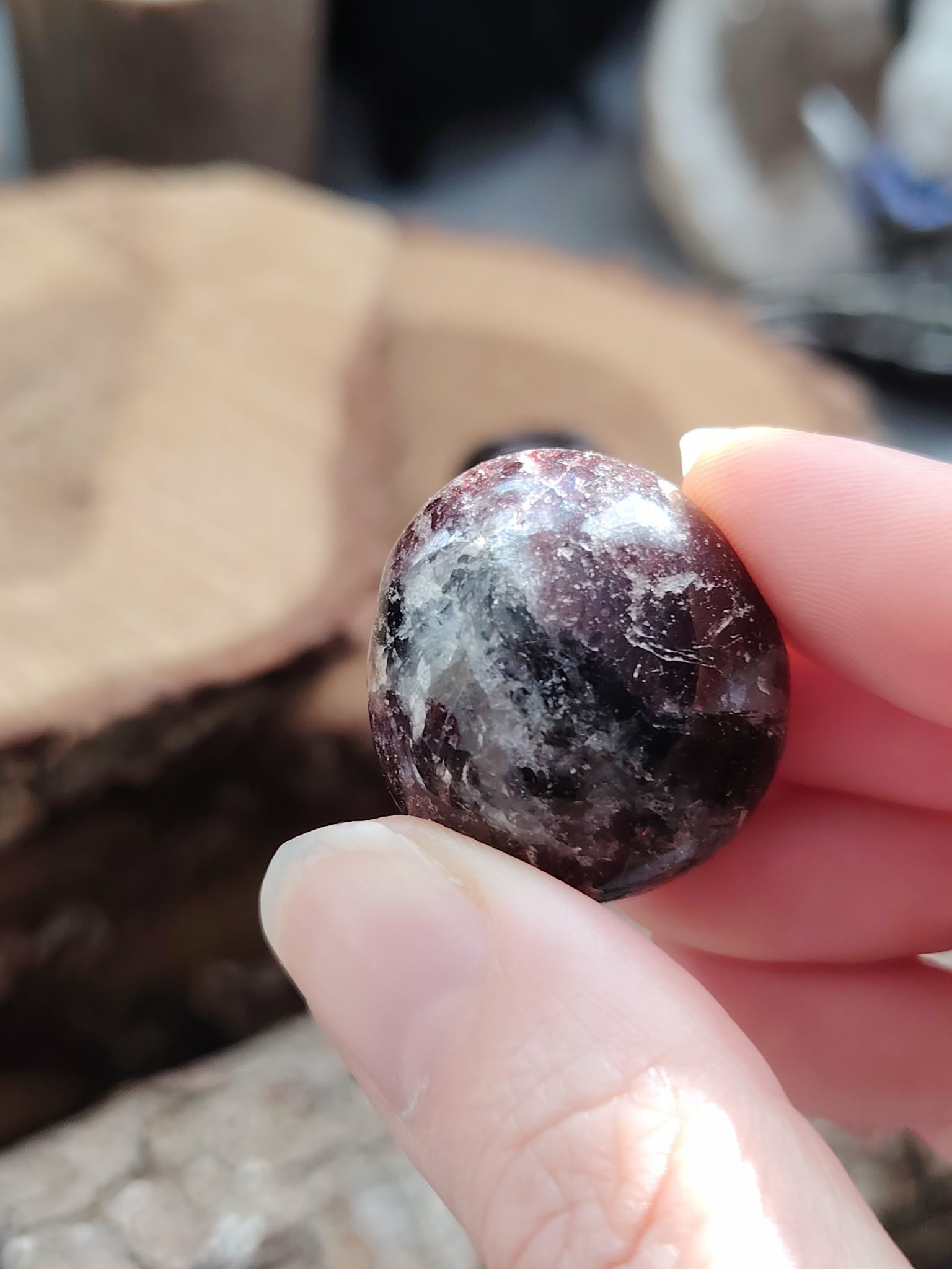 Pierre roulée de grenat almandin rouge sombre tenue entre deux doigts, surface polie aux reflets profonds, pierre naturelle associée à l’assurance, à la solidité et à l’élan vital.