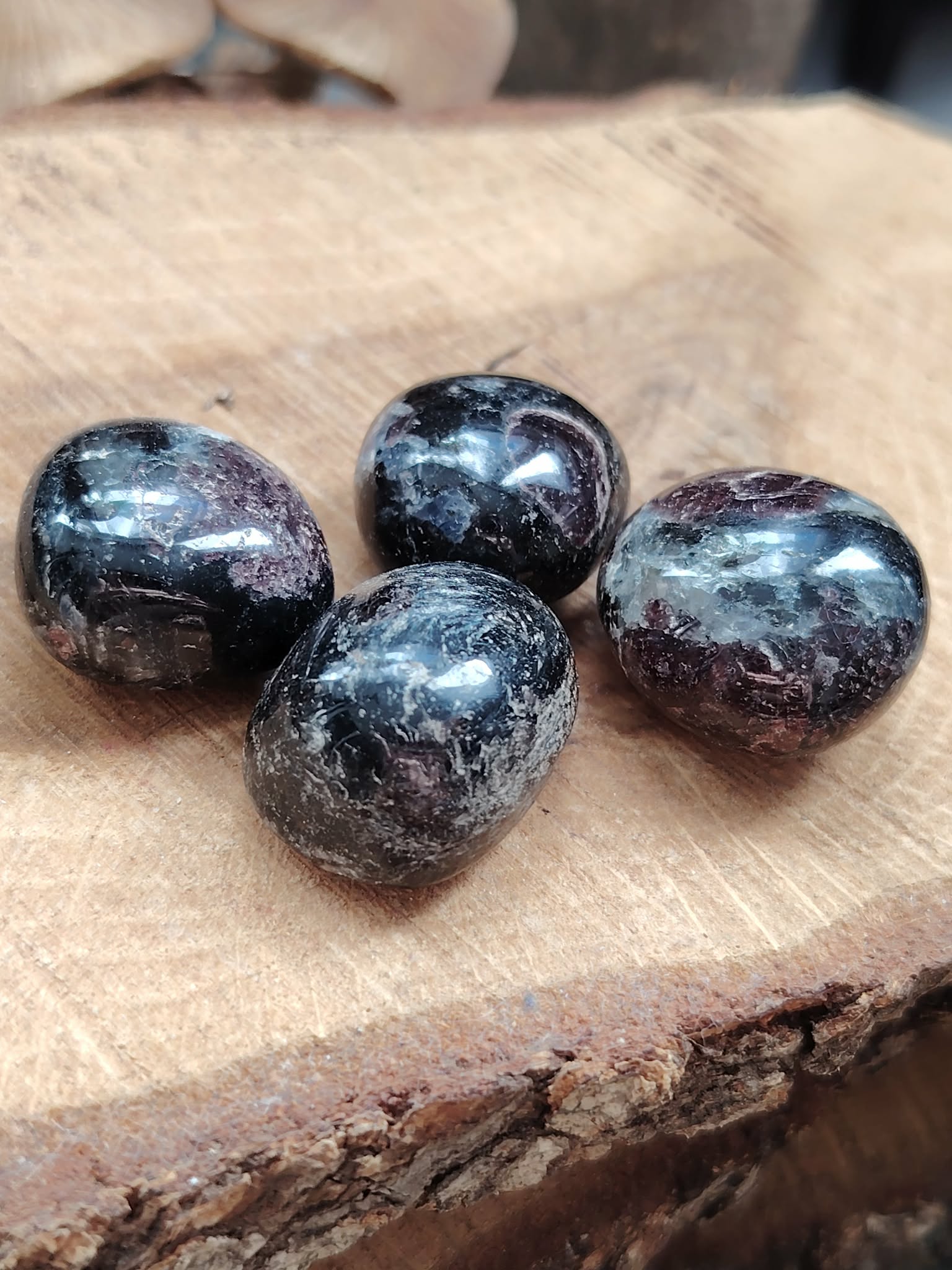 Quatre pierres roulées de grenat almandin rouge sombre posées sur une tranche de bois, pierres naturelles associées au courage, à la persévérance et à l’équilibre intérieur.