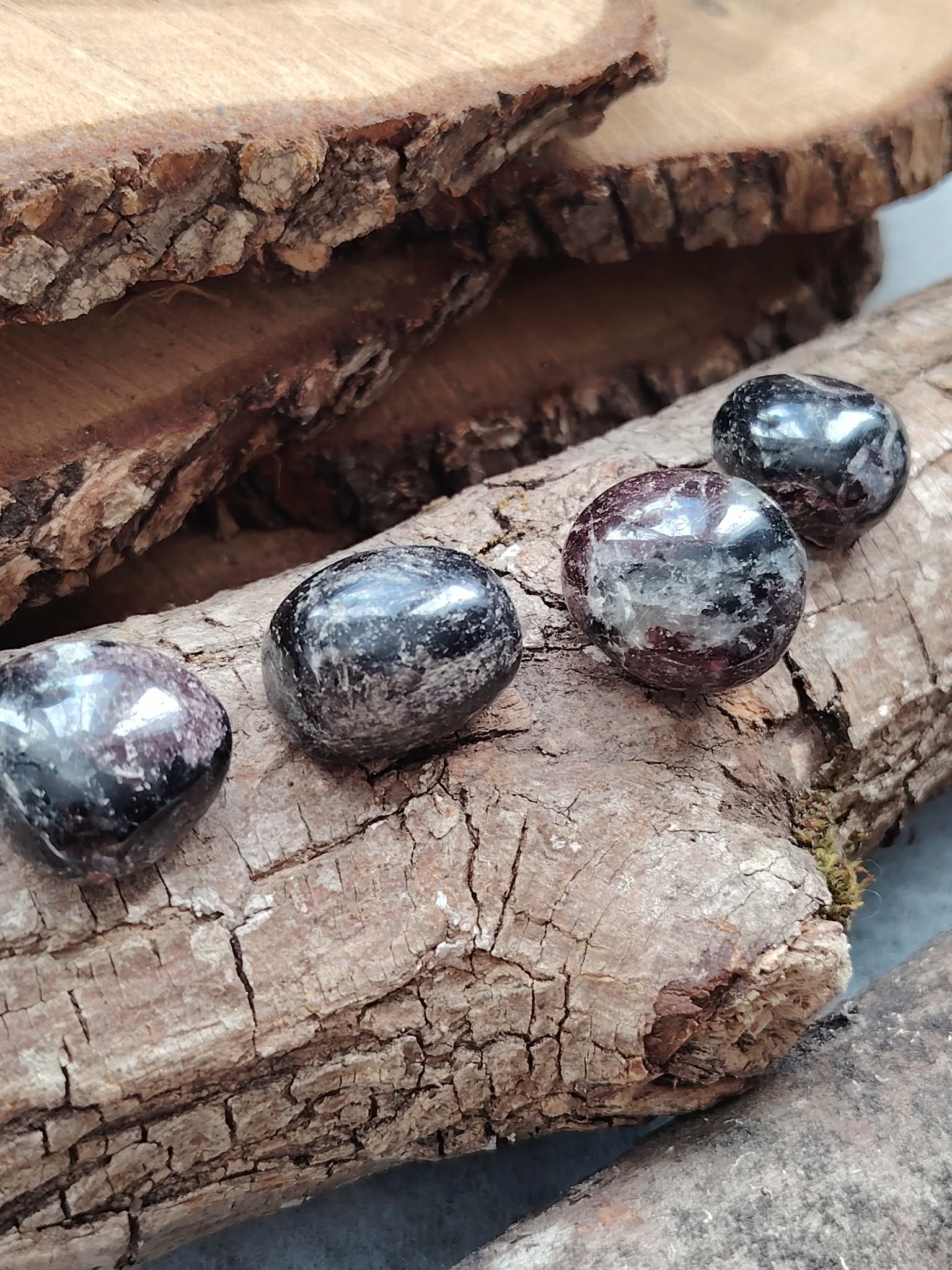 Pierres roulées de grenat almandin rouge sombre posées sur bois naturel, reflets profonds et texture polie, pierres naturelles évoquant la confiance calme, la présence à soi et l’énergie stable.
