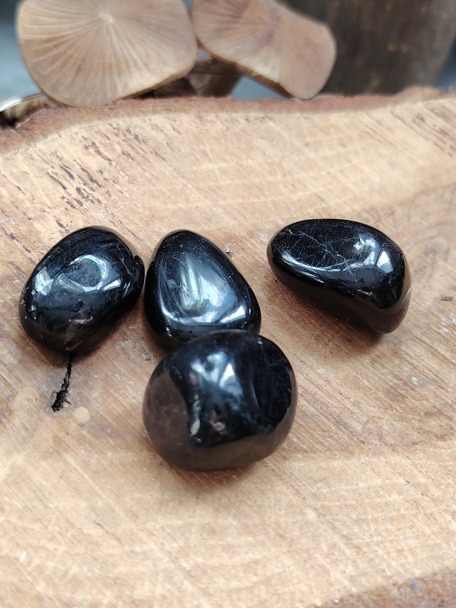 Quatre pierres roulées d’hyperstène noir brillant posées sur une tranche de bois, reflets profonds, pour inviter à l’ancrage, la protection et la clarté mentale.